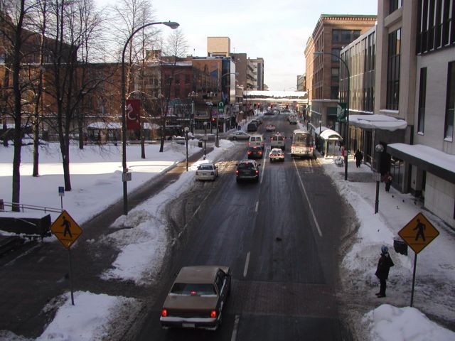 Photo Shot from S Clinton Ave while in a section of the 'Skyway' similar to the structure connecting the buildings in the background, hovering over the N Clinton Ave side of E Main St. Not visible, Linconln Tower would be on the left and the proposed 'Transportation Center' would clear out many of the buildings now visible in the left background.  Midtown Plaza on the right, with the Sibley building on the other side of E Main Street. Snow covered Rochester NY New York City living January 26th 2003 POD I Love NY Rochester NY New York winter Picture Of The Day view picture photo image pictures photos images, January 26th 2003 POD