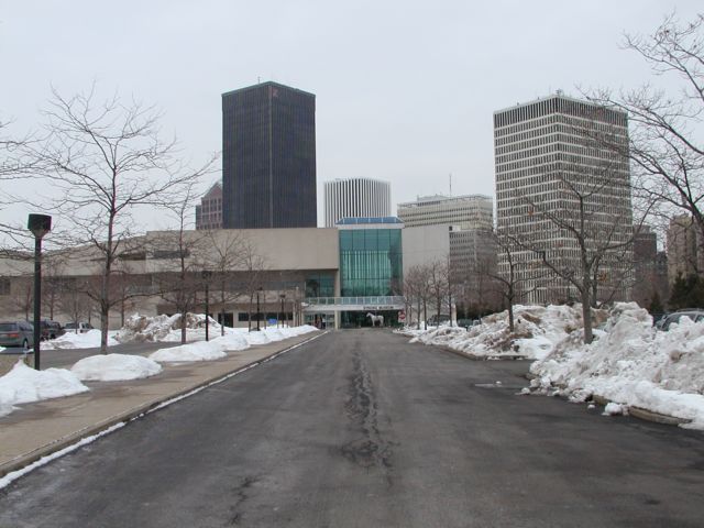 Picture Winter's leafless trees and snow banks line the path to the Strong Museum. One of the Horse's on Parade family waits at the entrance with the Rochester NY skyline in the background. Bausch and Lomb, Xerox, Lincoln Tower, Midtown Plaza, HSBC all visible. Rochester NY winter view. Rochester NY March 11th 2003 POD winter Picture Of The Day view picture photo image picture pictures photos images