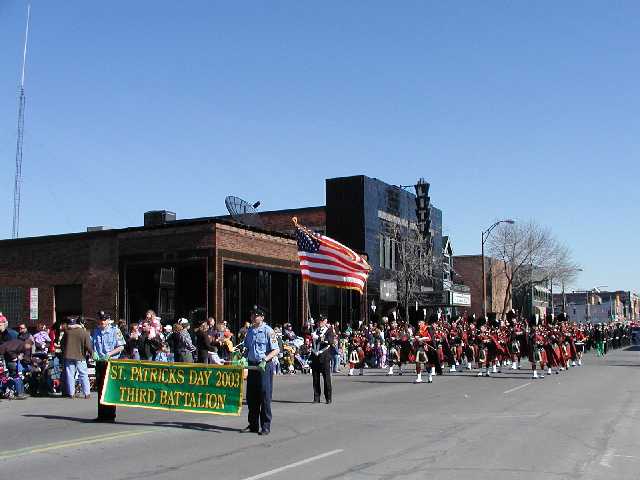 Picture Third Battalion Firefighters make their way up East Avenue with a Saint Patrick's Day banner followed by a Color Bearer and a Bagpipe unit. An appreciative crowd lines East Ave near the Little Theatre. Shot Saturday March 15th 2003. East Ave looking east. Rochester NY March 17th 2003 POD winter Picture Of The Day view picture photo image picture pictures photos images