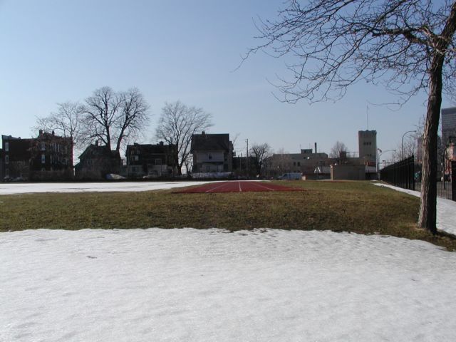 Picture Snow recedes from the playing field at the Monroe Middle School, revealing the soft, muddy, lawn, and the smooth surface of the running track. The background is siloheted by residential homes, apartments, buildings, and a few towering leafless trees. Rochester NY March 18th 2003 POD winter Picture Of The Day view picture photo image picture pictures photos images