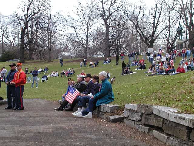 A Marine stands with another veteran while a small group of veterans and family sit along the south edge of the Highland Park concert shell. The growing crowd in the background is there in a show of caring, love, and support for U.S., and all troops engaged in the global war on terrorism Image 16 of 60  -  68 kB