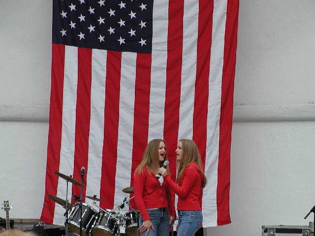 American Twins, Rhian and Cara Morgan, Rochster NY area locals of American Idol fame, lead an appreciative audiance in the American National Anthem during the Rally 'Round America celebration held in Highland Park, Rochester NY, Saturday, April 19th, 2003.  Image 36 of 60  -  30 kB